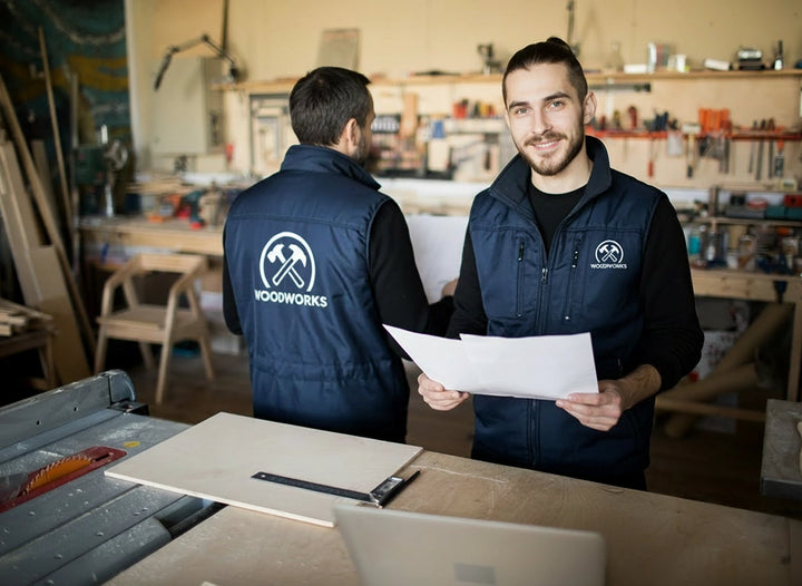 Deux menuisiers de wodworks Pornic dans leur atelier de dos et de face avec des vestes de travail logotées par Pop'Art Design